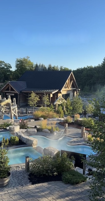 Nature spa with outdoor heated pools, wooden cabins with saunas and lush greens, with steam coming up from the heated pools.
